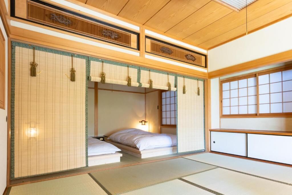 Una habitación japonesa tradicional con suelo de tatami, cama de madera baja, puertas correderas y un mamparas shoji.