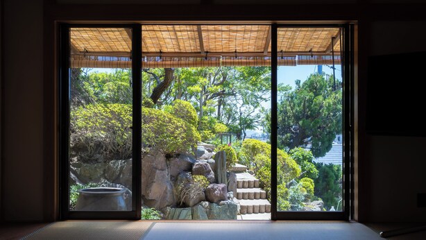 A traditional Japanese room with tatami flooring, a shoji screen door, and a view of a garden with rocks, trees, and a koi pond. - HABi-Wakaura (Wakayama)