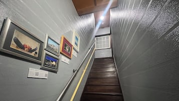 A staircase with wooden steps and metal railings, leading to a landing with framed pictures on the walls.
