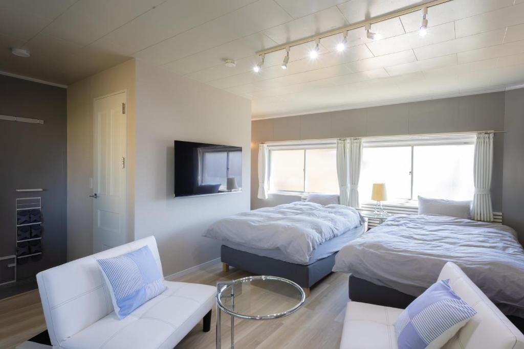 A modern hotel room with two beds, a TV, and a seating area with a round table.