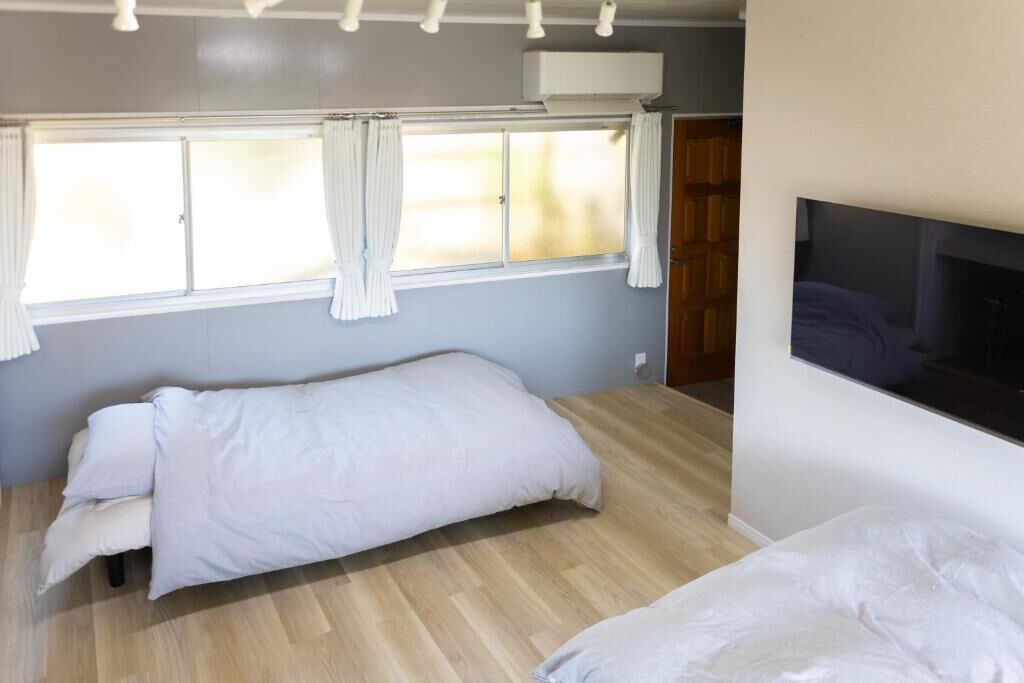 A bedroom with a bed, a window with curtains, a wall-mounted TV, and a wooden door.