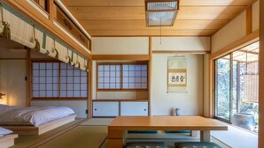 A traditional Japanese room with tatami flooring, a low wooden table, a futon bed, sliding shoji doors, and a view of the outdoors. - HABi-Wakaura (Wakayama)