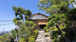 A traditional Japanese house with a wooden exterior, surrounded by lush greenery and a stone staircase leading to the entrance. - HABi-Wakaura (Wakayama)