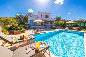 A poolside area with lounge chairs, a barbecue, and a house in the background. - Villa Aspa in Prines (Rethymno)