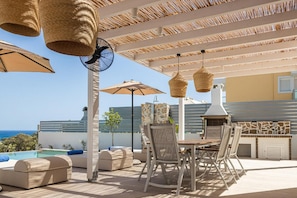 Eine Terrasse im Freien mit Tisch, Stühlen, einem Grill und Sonnenschirmen.