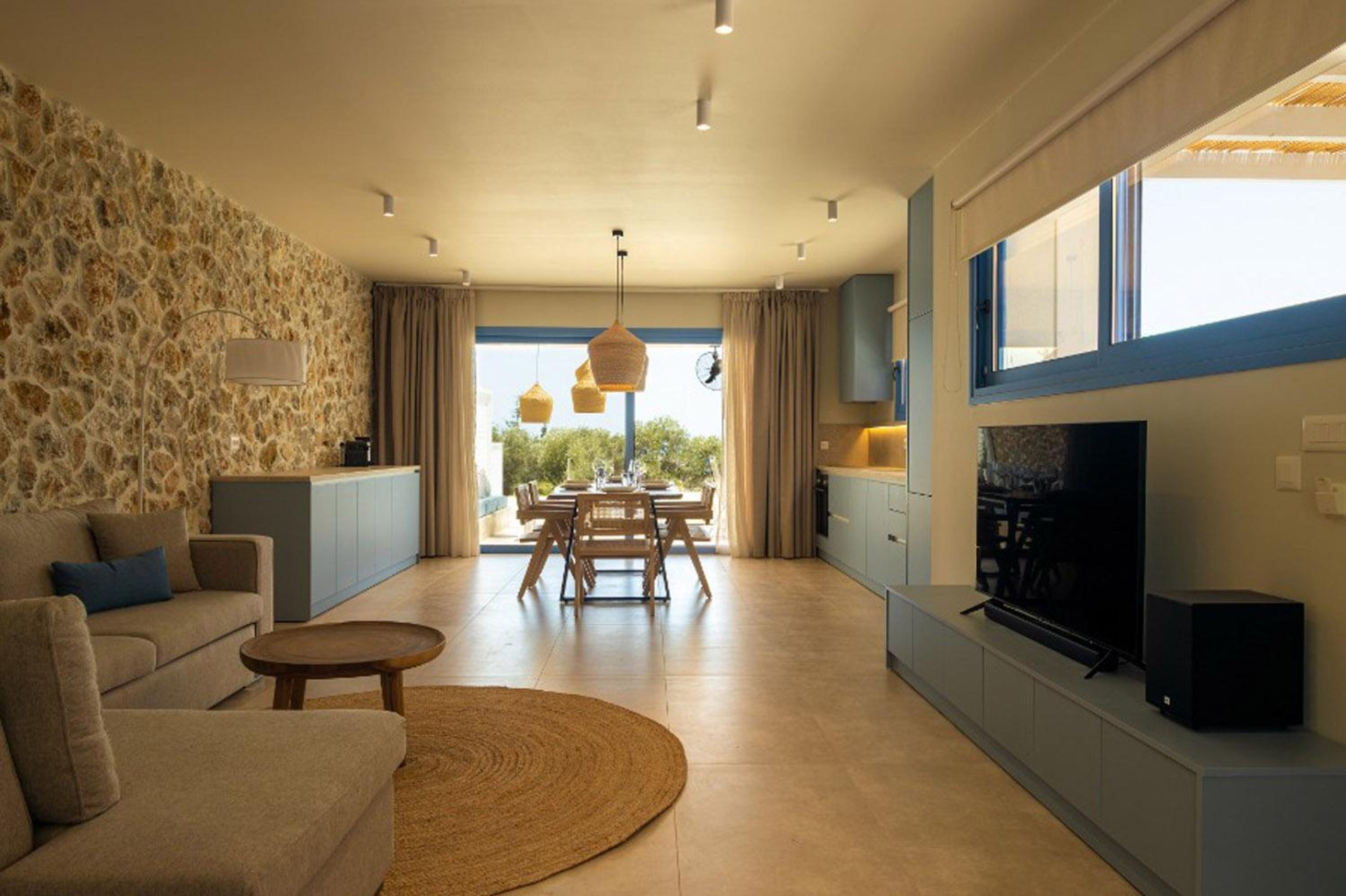 Un salon moderne avec un mur en pierre, un canapé, une table basse, un coin repas et un téléviseur.