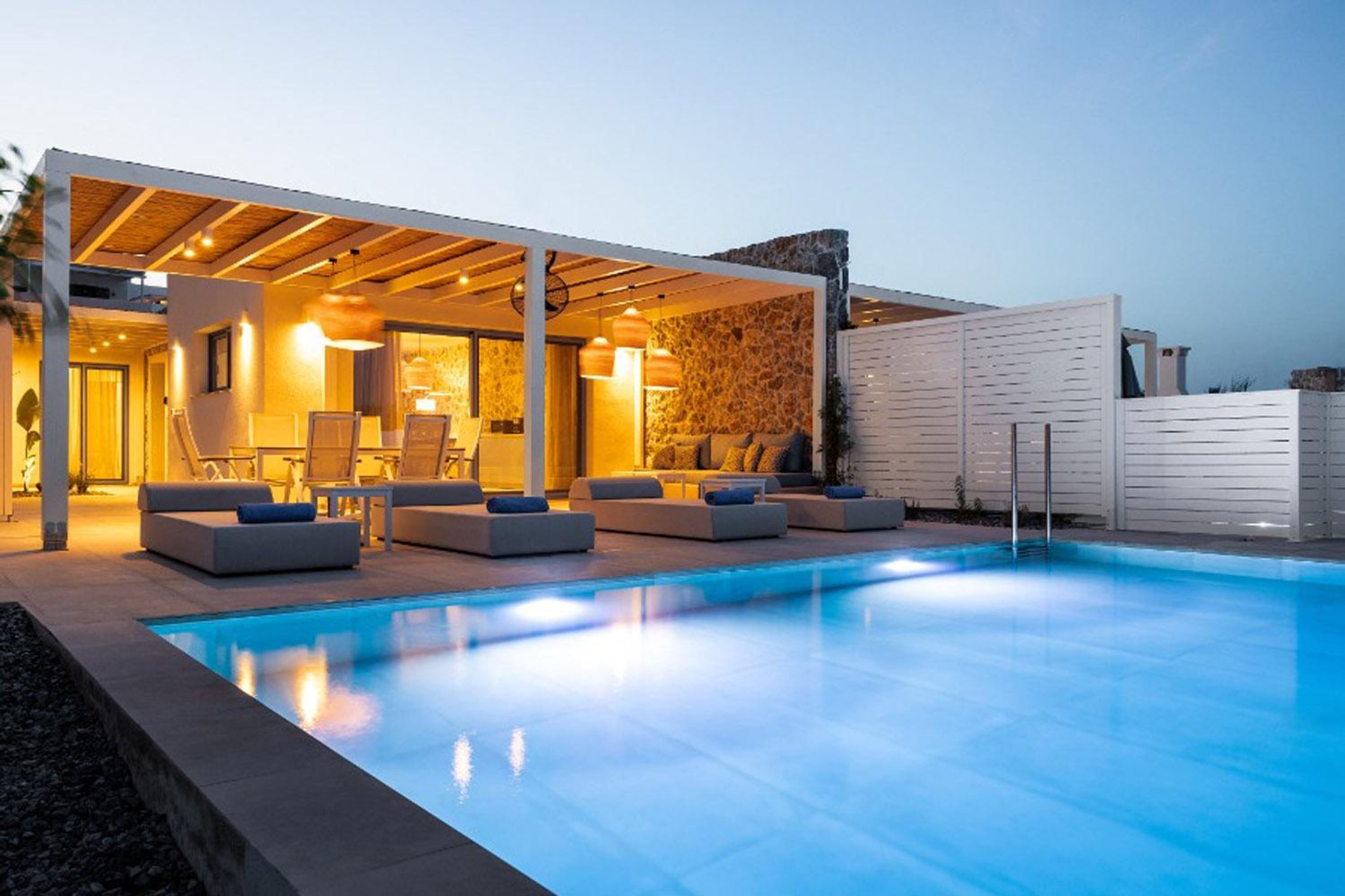 Ein moderner Poolbereich im Freien mit überdachter Lounge-Ecke und einer Wand aus Stein im Hintergrund.