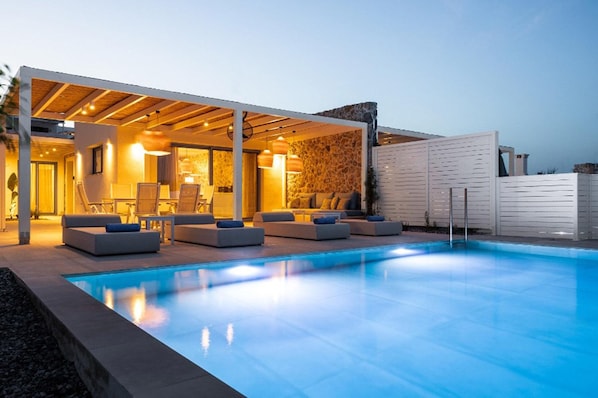 Ein moderner Poolbereich im Freien mit überdachter Lounge-Ecke und einer Wand aus Stein im Hintergrund.