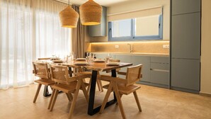 A modern dining area with a wooden table and chairs, a kitchen with blue cabinets, and a large window with sheer curtains.