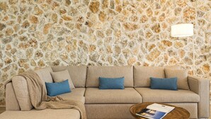 A living room with a stone wall, a beige sofa, blue cushions, a wooden coffee table, and a floor lamp.