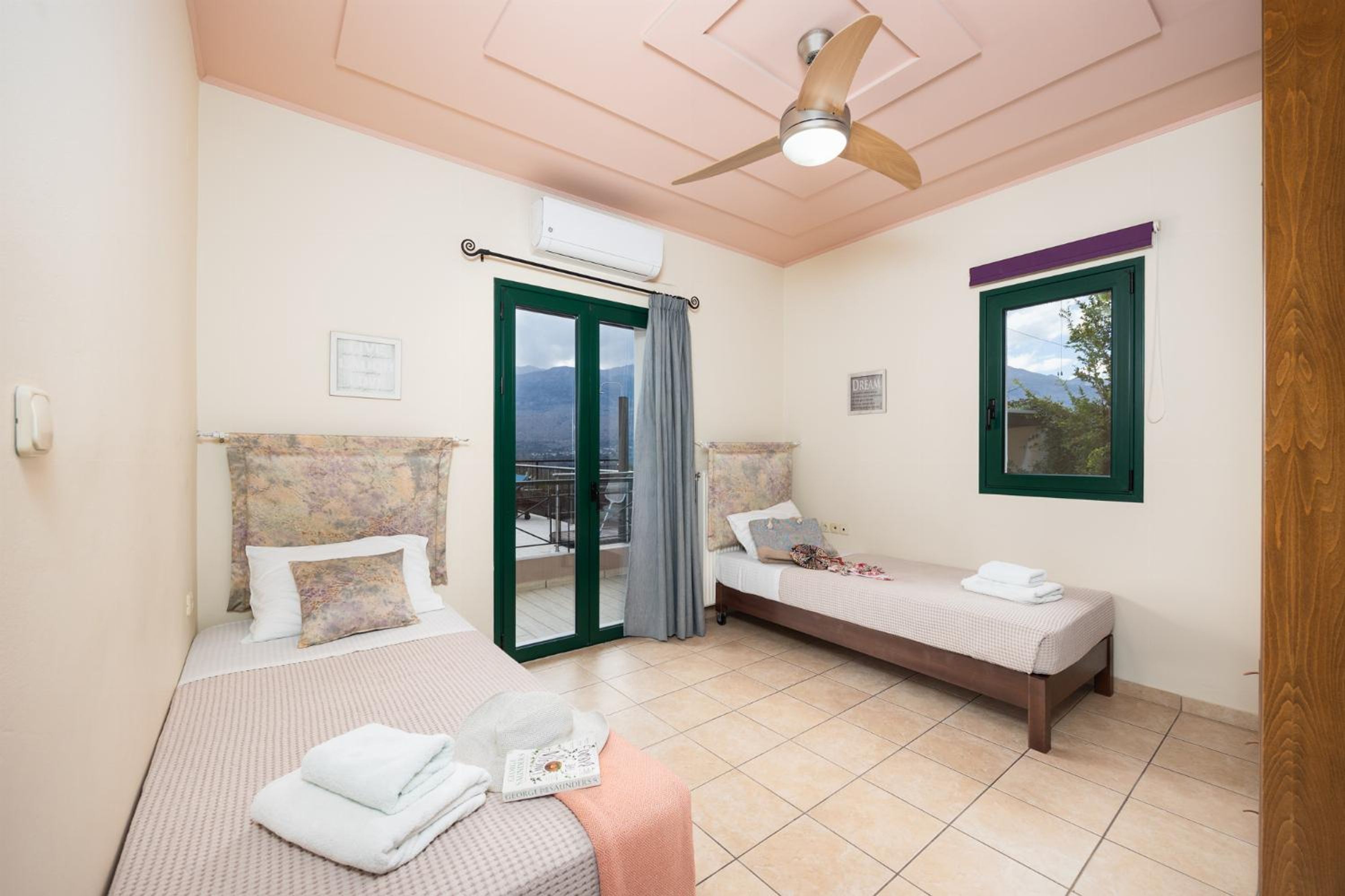 Ein Hotelzimmer mit zwei Betten, einem Deckenventilator, einer Klimaanlage, einem Fenster mit Blick und einer Tür zu einem Außenbereich.
