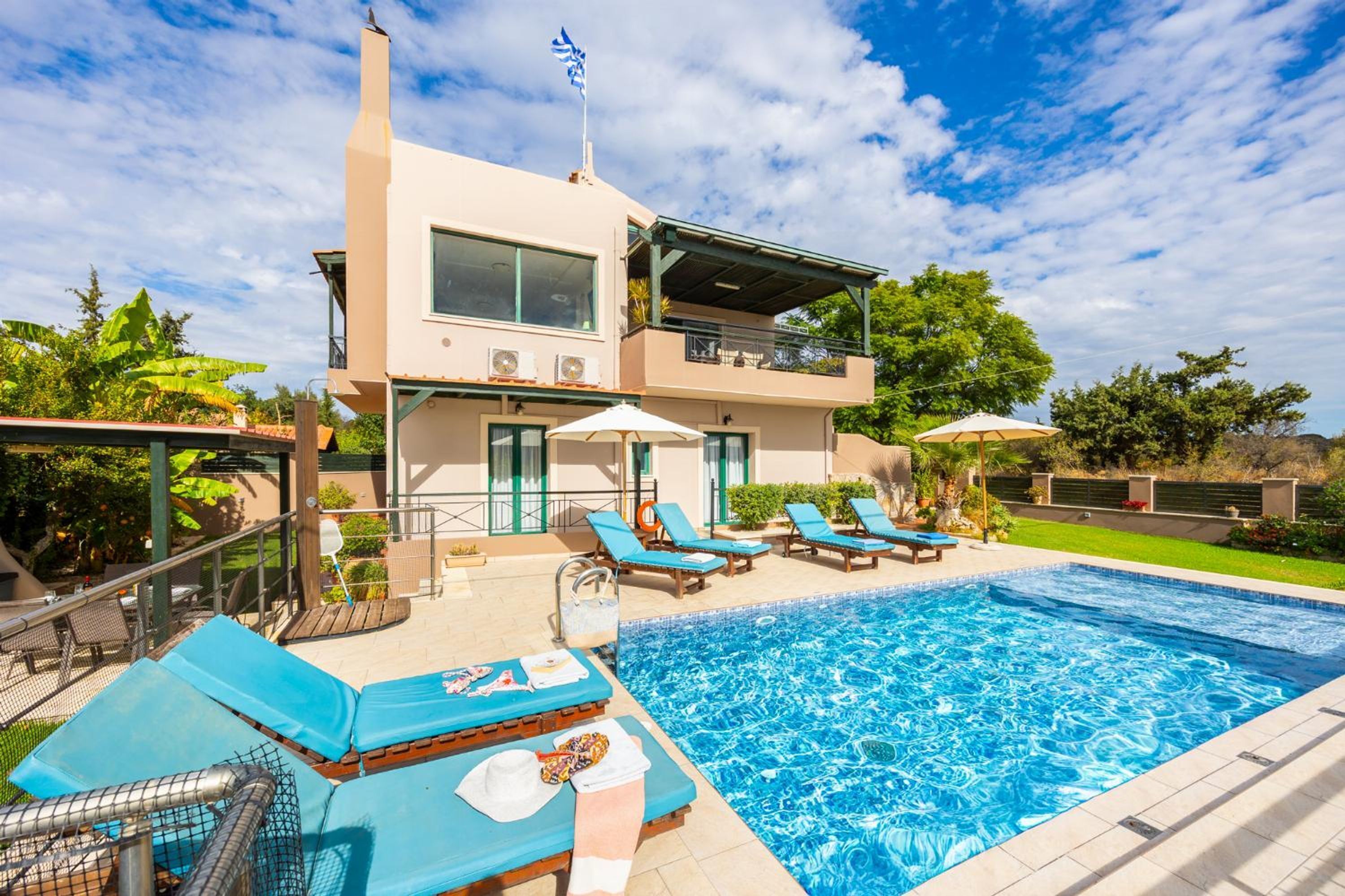 A modern two-story building with a swimming pool, sun loungers, and a covered outdoor area.