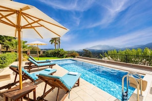 Un espace piscine agrémenté de chaises longues et de parasols, entouré de verdure et offrant une vue sur les montagnes.