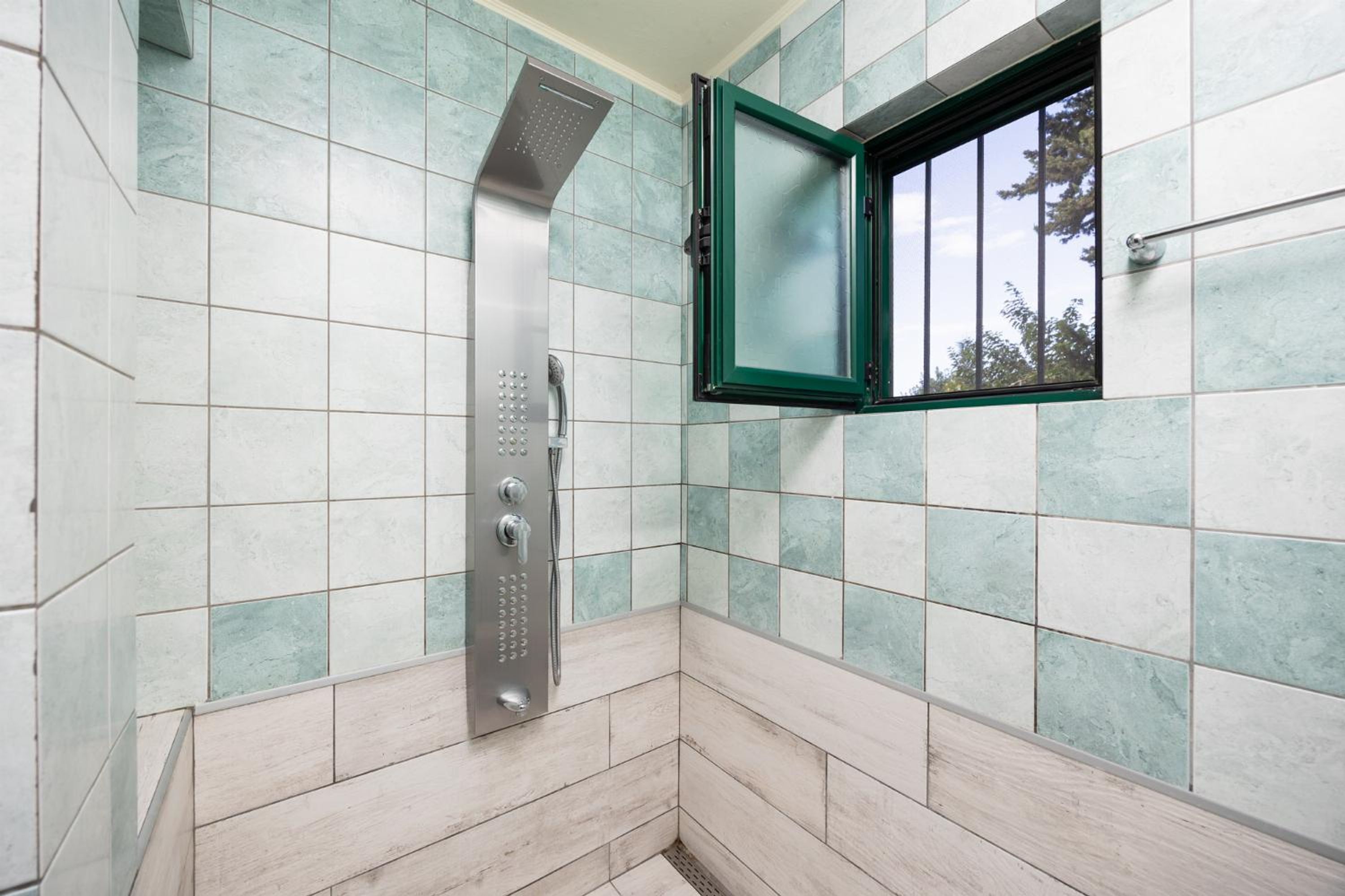 A shower with a rain showerhead and a window with a green frame.