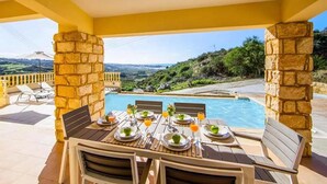 A dining table set for four with a pool view, stone pillars, and a yellow ceiling. - Villa Aqua View in Kissonerga (Pegeia)
