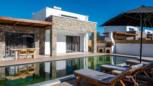 A modern poolside area with lounge chairs and a dining table. - Villa Aurelia in Afandou (Rhodes)