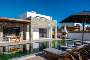 Zona de piscina moderna amb gandules i una taula de menjador.