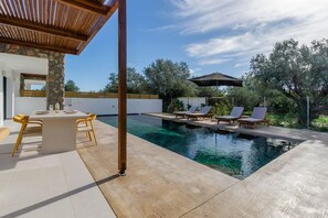 A modern outdoor pool area with a pergola, lounge chairs, and a dining table. - Villa Amethysta in Afandou (Rhodes)