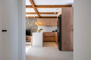 A modern kitchen with wooden cabinets, a central island, and a stone accent wall. - Villa Amethysta in Afandou (Rhodes)