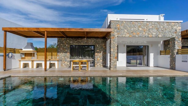 Une maison moderne avec une façade en pierre, une piscine et un espace salon extérieur.