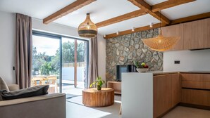 Un salon moderne comprenant un canapé, une table basse ronde en bois et un coin cuisine avec des meubles en bois et un mur en pierre.