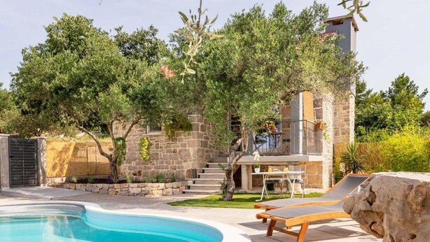 A pool area with lounge chairs, a stone building with a staircase, and surrounding greenery. - Villa Bella Vista in Sveti Filip i Jakov (Sveti Filip i Jakov)