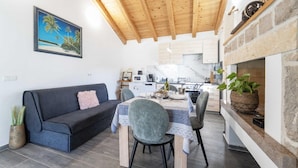 A cozy living area with a dark blue sofa, a dining table with chairs, and a kitchen in the background. - Villa Bella Vista in Sveti Filip i Jakov (Sveti Filip i Jakov)