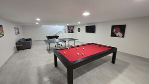 Et billardbord med kugler, en sofa, et bordtennisbord og kunst på væggene.