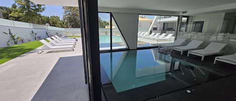 Une piscine intérieure moderne avec des parois en verre, des chaises longues et une vue dégagée sur l’espace extérieur de la piscine.
