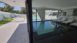 Ein moderner, überdachter Pool mit Glaswänden, Liegestühlen und freiem Blick auf den Außenbereich.
