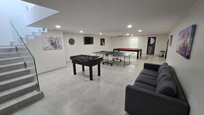 Ein modernes Wohnzimmer mit Kicker, Billardtisch und einer Treppe.