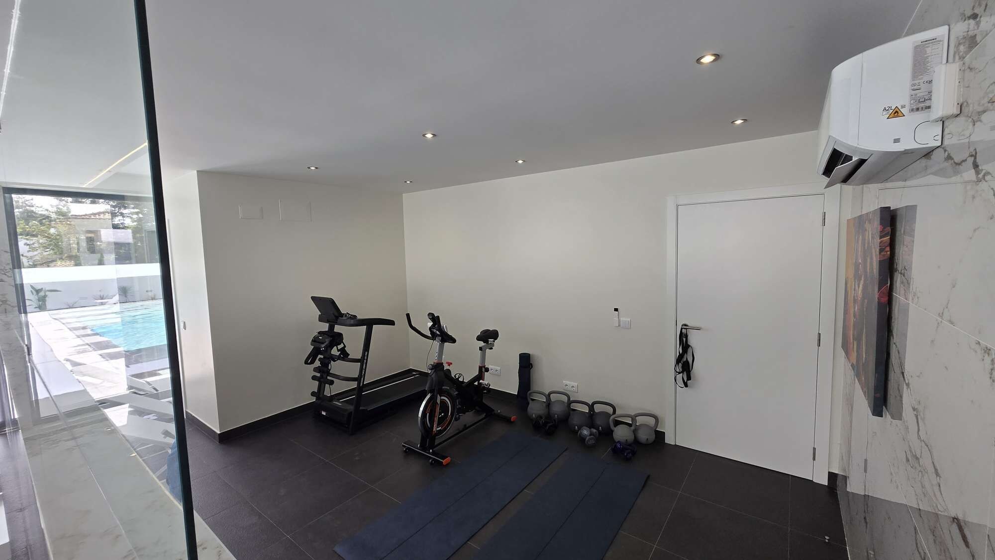 A modern home gym with exercise equipment, a yoga mat, and a view of a swimming pool.