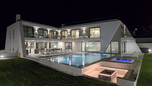 Et moderne hus med to etager, swimmingpool, udendørs møbler og et godt oplyst interiør.