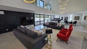 Ein modernes Wohnzimmer mit einer Couch, roten Sesseln, einem Fernseher und einem Essbereich mit Tisch und Stühlen.