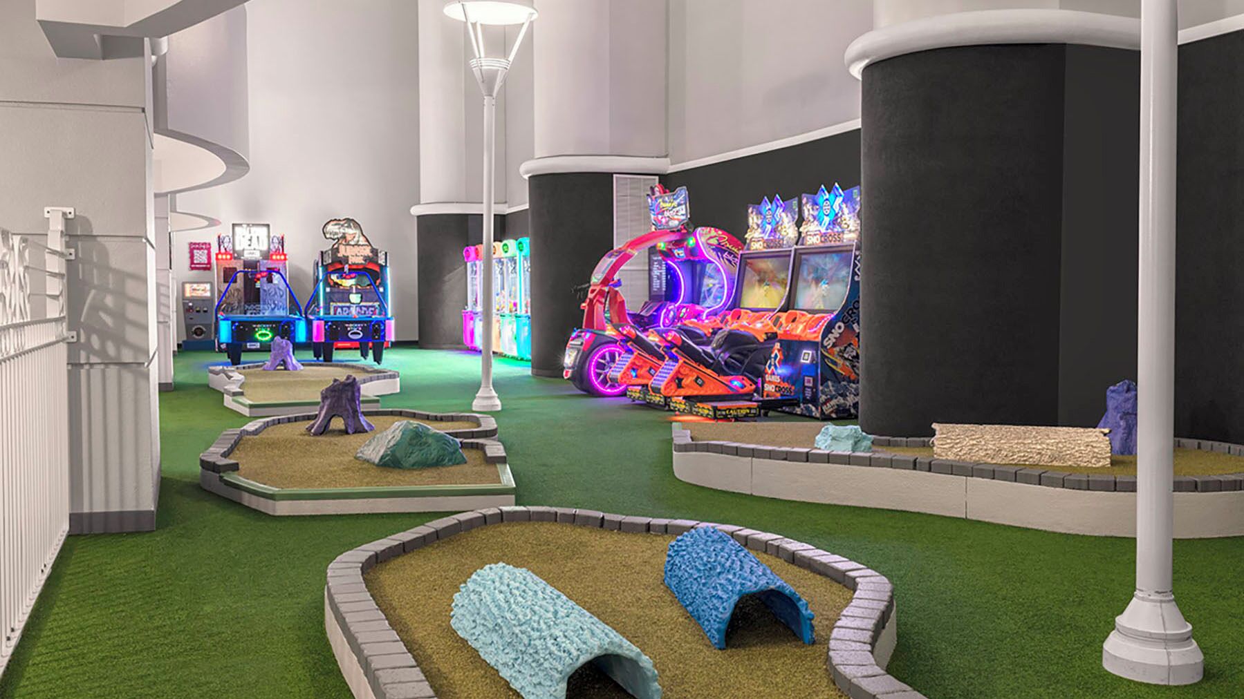 A brightly lit indoor play area with arcade games, a neon motorcycle, and a small garden with a tree stump and a blue tunnel.