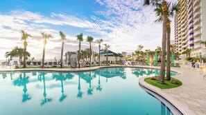 Una piscina de resort con palmeras, sillas de descanso y un rascacielos al fondo.
