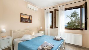 A bedroom with a bed, a nightstand, a window with curtains, and a painting on the wall. - Villa Elpida in Gaios (Paxos)