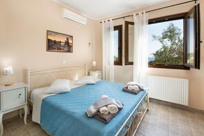 Ein Schlafzimmer mit Bett, Nachttisch, einem Fenster mit Vorhängen und einem Gemälde an der Wand.