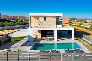 Ein modernes, zweistöckiges Haus mit Swimmingpool, Sitzgelegenheiten im Freien und Blick auf die umliegende Landschaft.