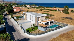 Ein modernes Haus mit Swimmingpool, umgeben von einem Zaun, mit Blick auf eine Küstenlandschaft.