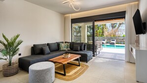 Ein modernes Wohnzimmer mit einem Ecksofa, einem Couchtisch aus Holz und einem großen Fenster mit Blick auf einen Pool.