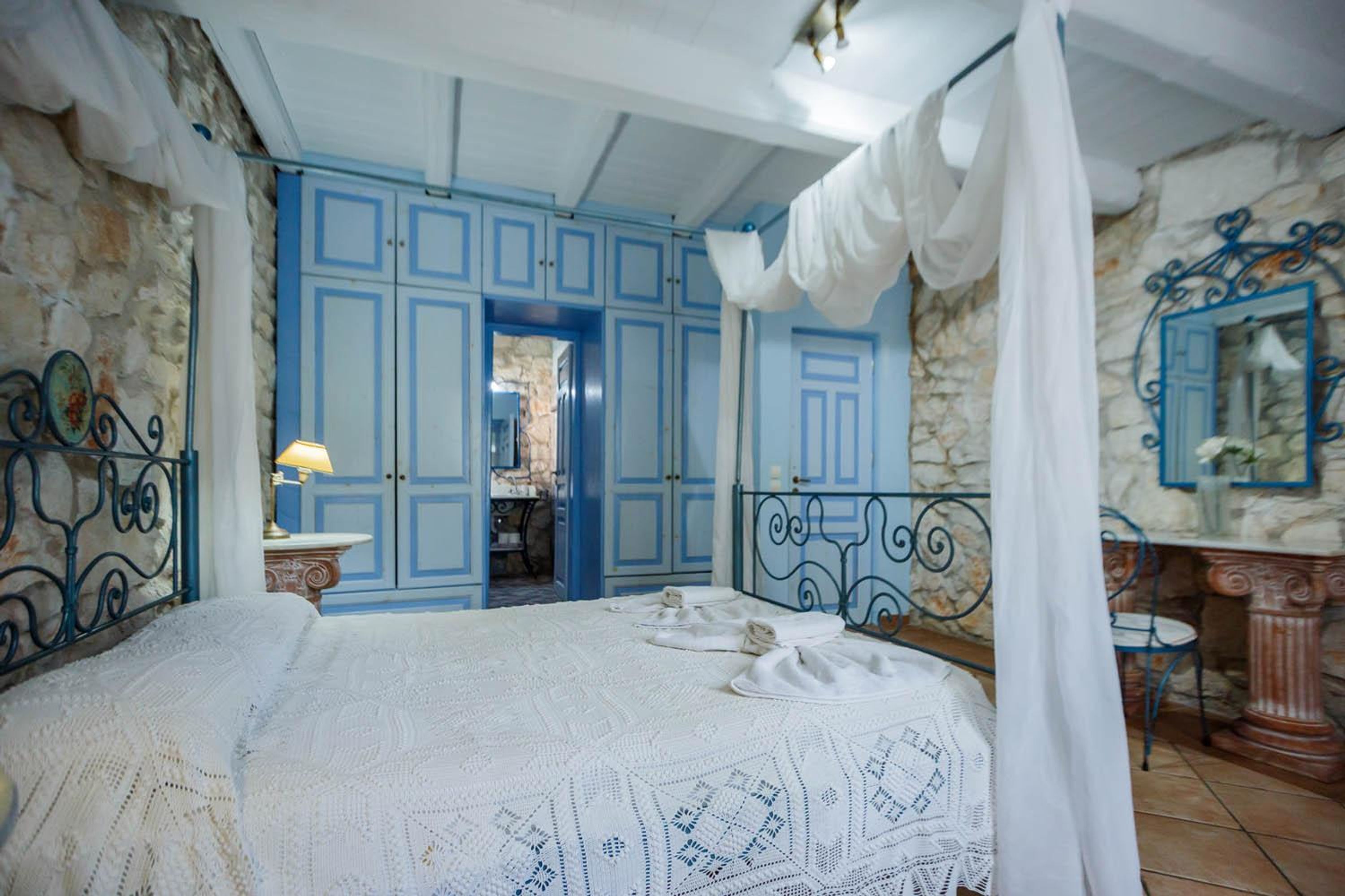 A bedroom with a large bed, blue cabinets, a stone wall, and a mirror.