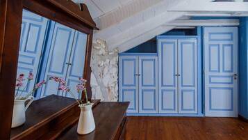 A room with a wooden dresser, a mirror, and a vase with flowers. There are blue doors and a stone wall in the background.