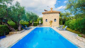 A swimming pool with lounge chairs, a stone building, and lush greenery.