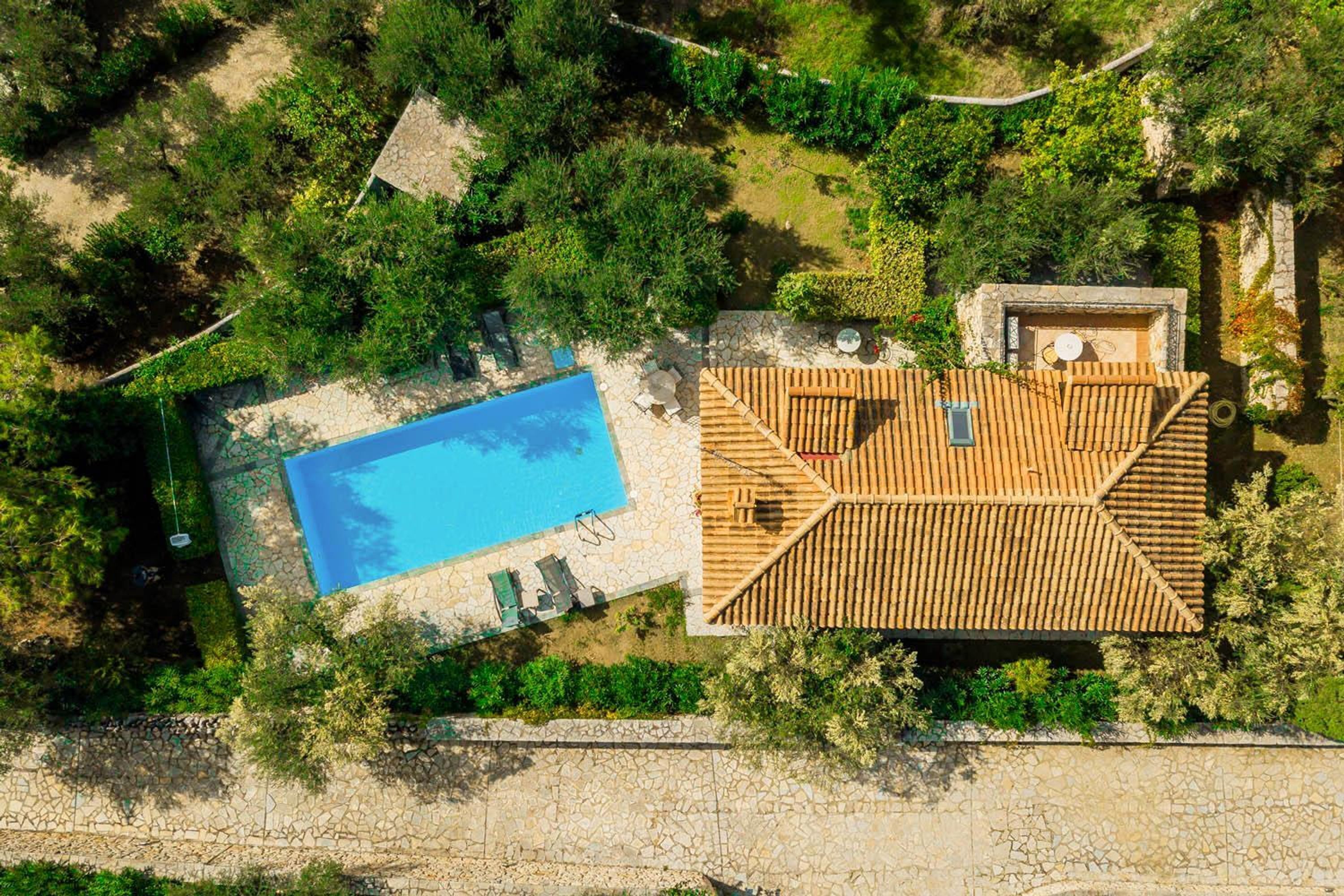 An aerial view of a property with a swimming pool, a wooden deck, and a stone wall.