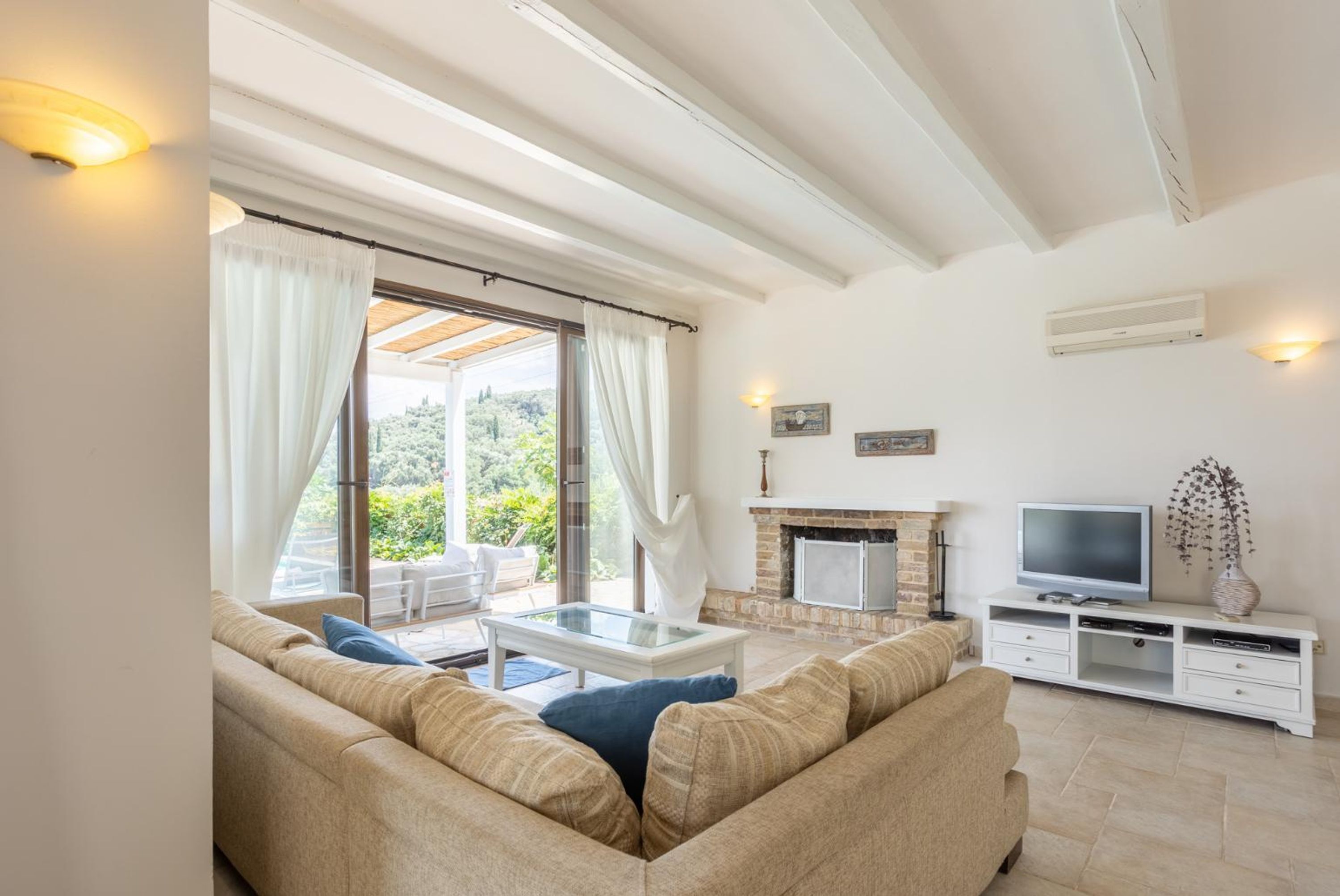 Een woonkamer met een bank, een salontafel met glazen blad, een open haard, een televisie en een balkon met gordijnen.