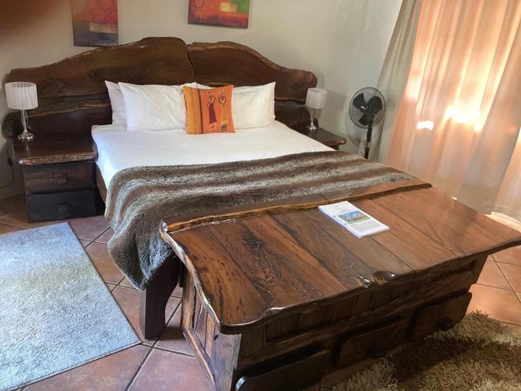 A bedroom with a wooden bed, a nightstand, a bedside table, a fan, and a rug.
