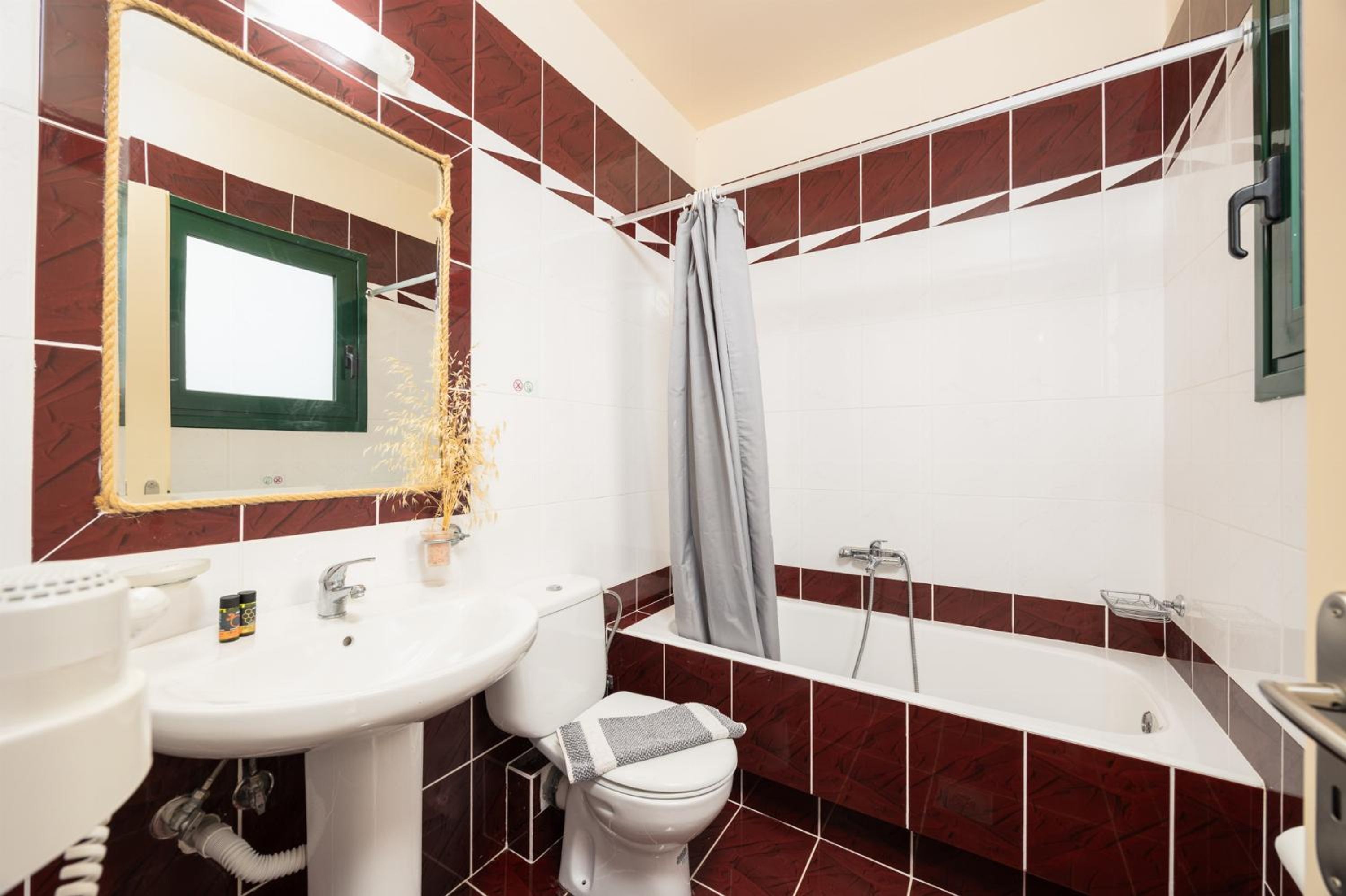 Casa de banho com lavatório, sanita e banheira, com azulejos vermelhos e brancos.