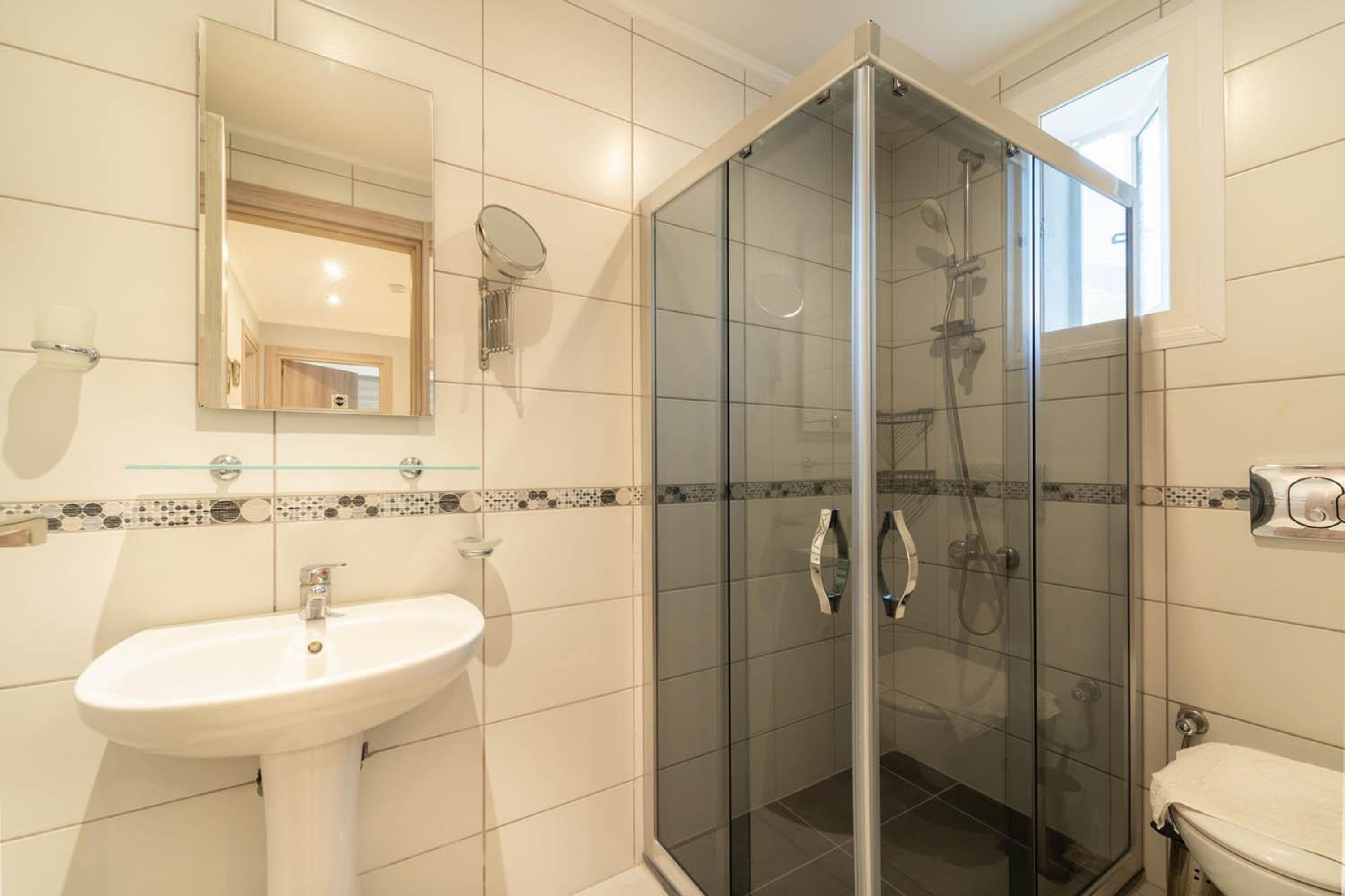 Un baño con ducha de mampara de vidrio, lavamanos pedestal y espejo.