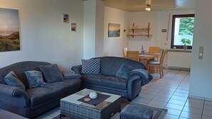 A living room with a sofa, a coffee table, and a dining area with a table and chairs. - Cozy vacation apartment quiet in Lindlar-Linde, approx. 30 km from Cologne (Lindlar)